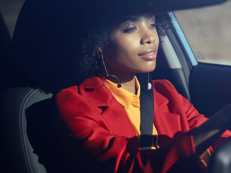 A woman sitting behind the wheel of her Hyundai KONA, looking very relaxed.  